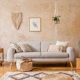 salon w stylu boho w odcieniach drewna z szarą kanapą na tle beżowej ściany