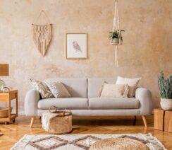 salon w stylu boho w odcieniach drewna z szarą kanapą na tle beżowej ściany
