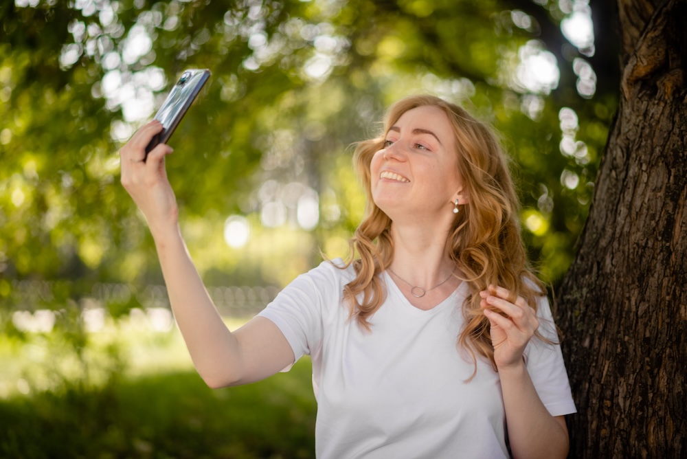 kobieta robiąca selfie pod drzewem 