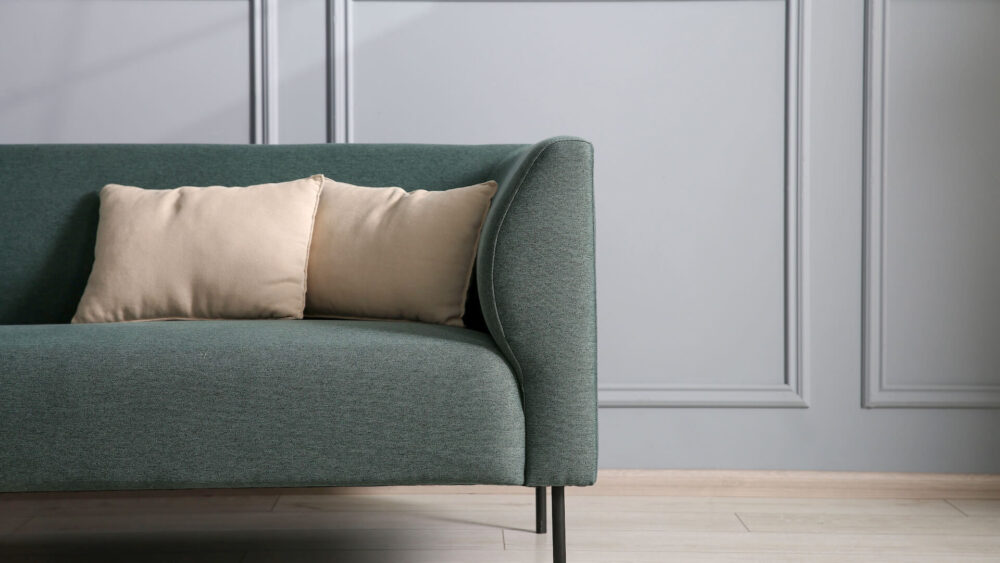 zielona sofa z beżowymi poduszkami w jasnym salonie