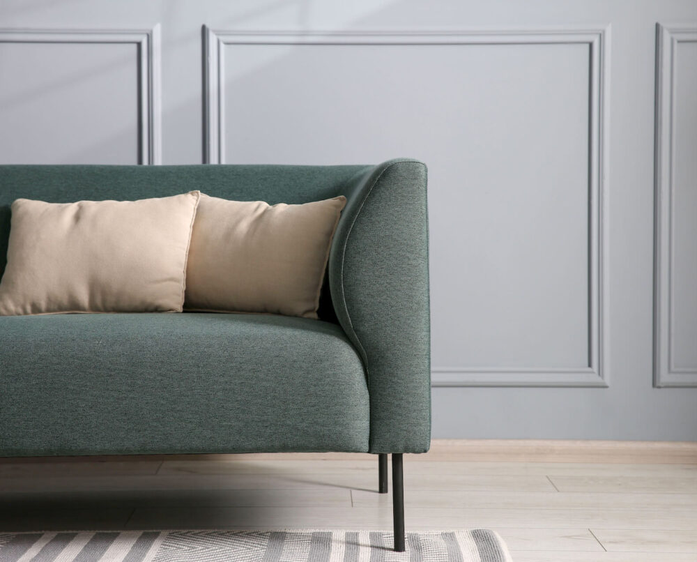 zielona sofa z beżowymi poduszkami w jasnym salonie