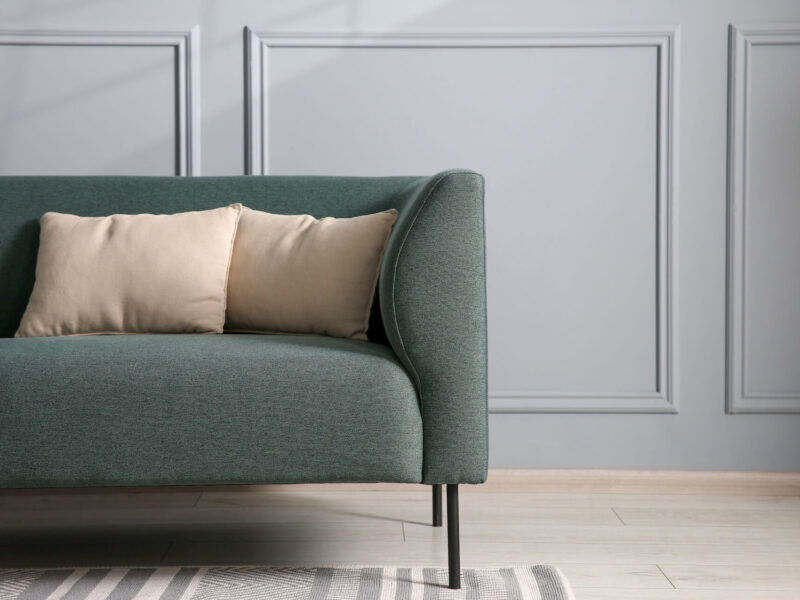 zielona sofa z beżowymi poduszkami w jasnym salonie